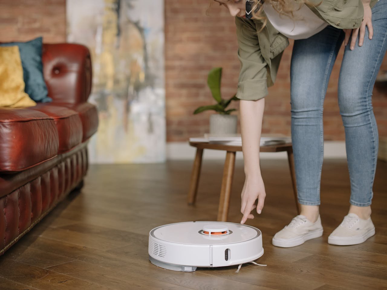 A woman in jeans interacts with a robotic vacuum cleaner in a cozy, stylish living room.